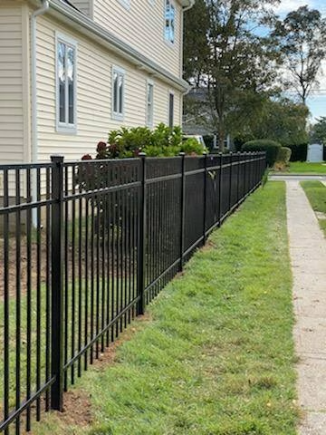 Black metal fence along a house and sidewalk, green lawn.