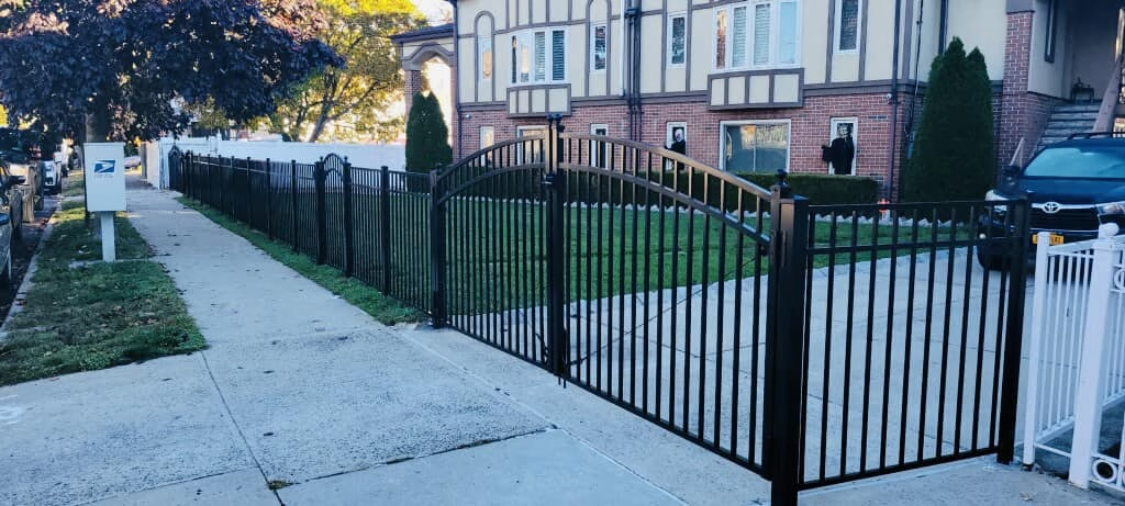 Black wrought iron gates open onto a walkway, leading toward a brick building.