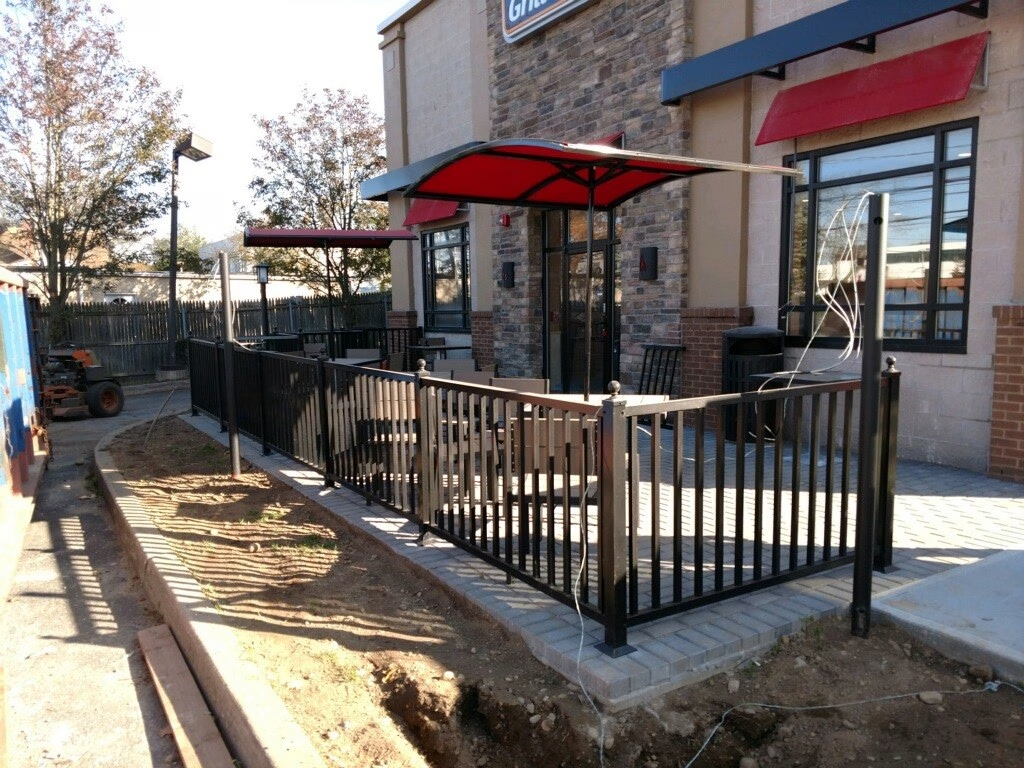 Outdoor dining area with black fence, red awnings, and tables in front of a restaurant.
