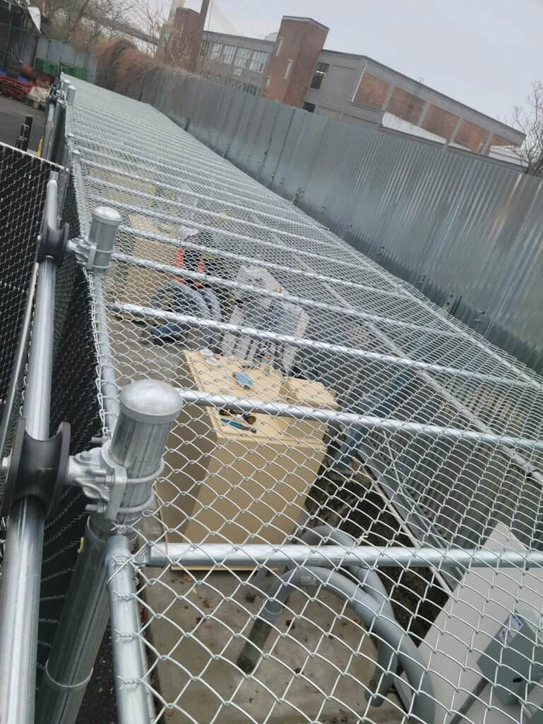 Overhead view of a chain-link fence structure protecting equipment in an outdoor industrial setting.