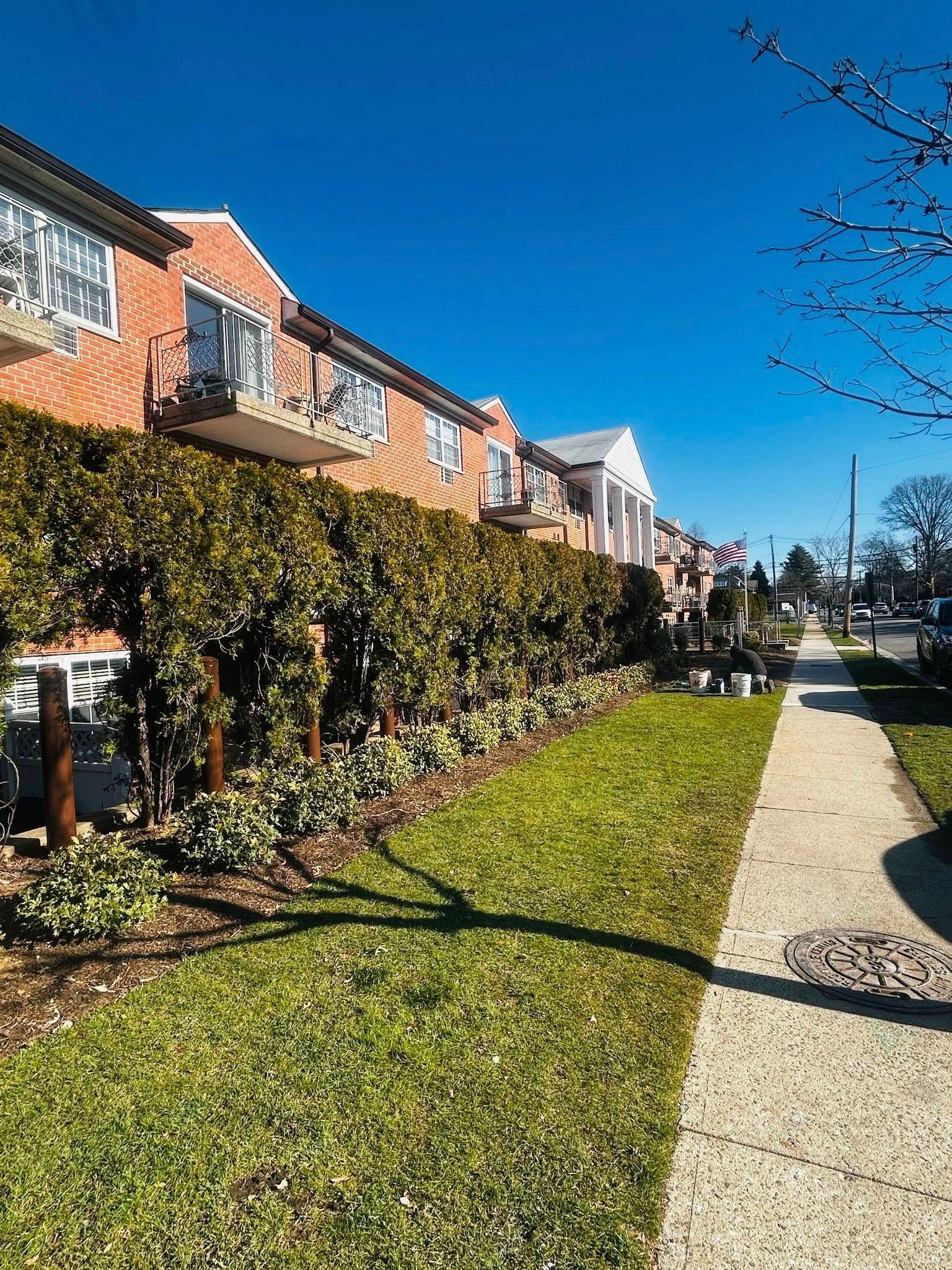 Row of brick buildings with balconies, a sidewalk, and green grass on a sunny day.