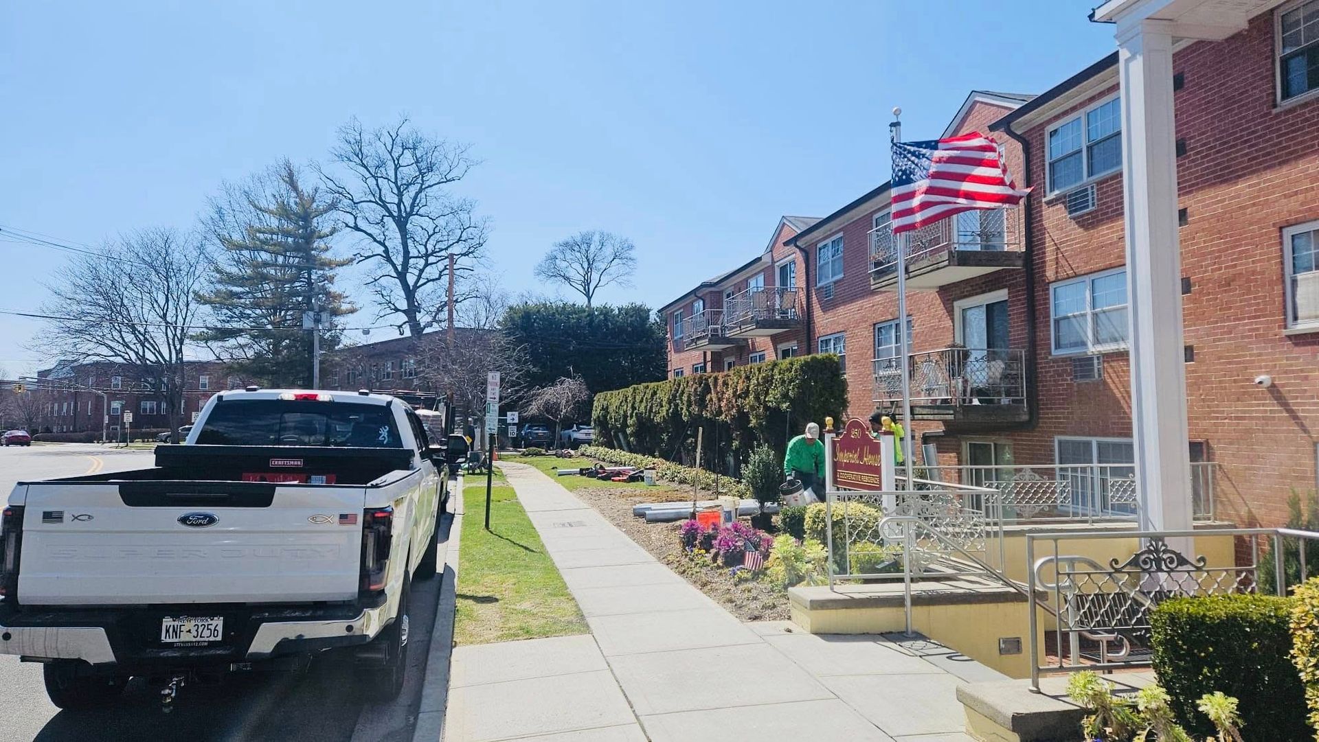 White pickup truck parked on street next to a brick building with an American flag.