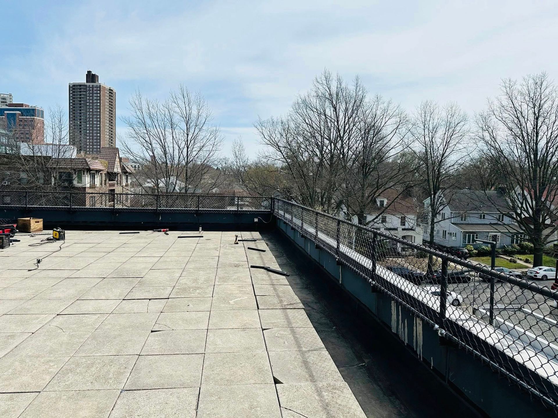 Rooftop view with dark fencing, trees, and buildings in the distance. Overcast sky.
