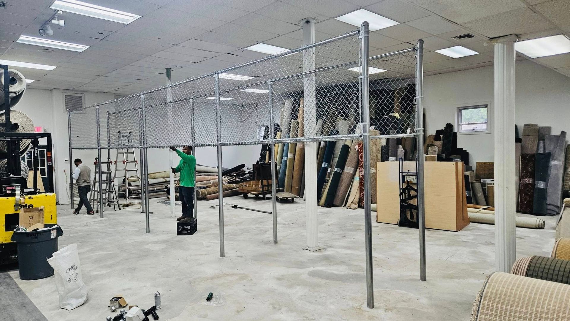 Workers installing a chain-link fence inside a commercial space with construction materials scattered around.