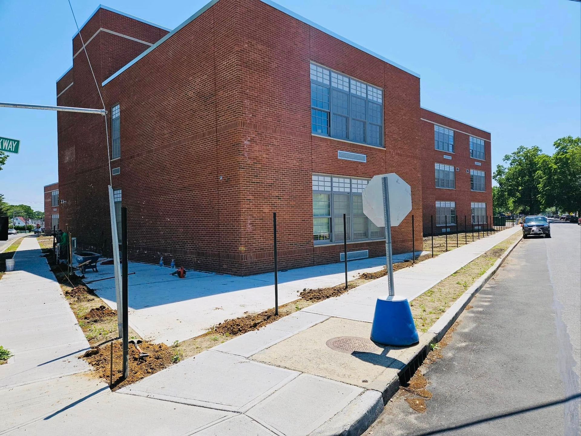 Brick school building on a sunny street corner, with sidewalks, signs, and a car in the distance.