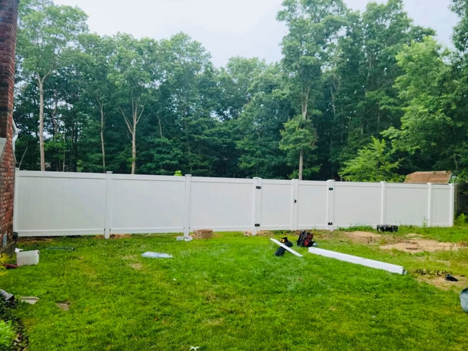 White vinyl privacy fence in a backyard, surrounded by trees.