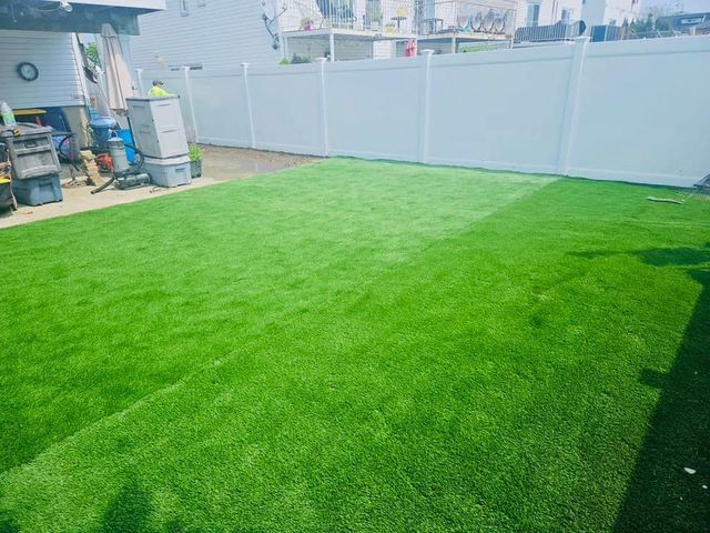 Backyard with bright green lawn, white vinyl fence, and patio equipment on the left.