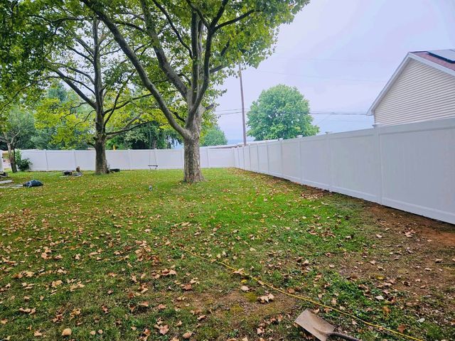 Backyard lawn with large trees, scattered leaves, and a white fence along the right side