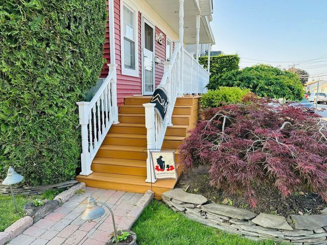 Front steps to a red house with a white railing, flanked by a green hedge and purple shrub.