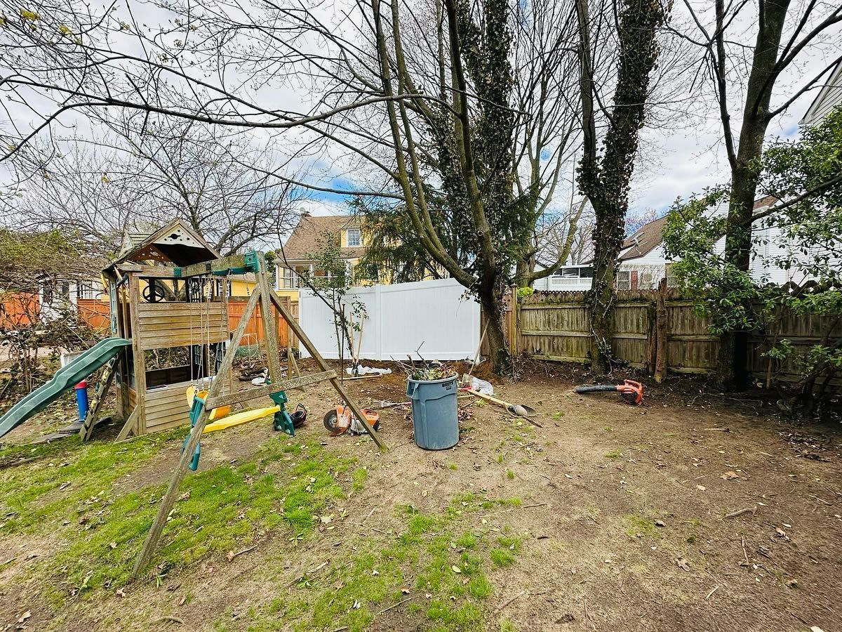 Backyard with wooden playset, blue slide, bare trees, white fence, wooden fence, and a white shed