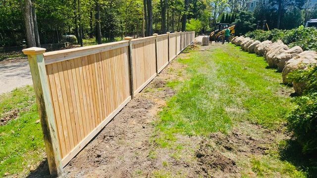 Wooden fence along a grassy path beside trees and rocks in a sunny outdoor area