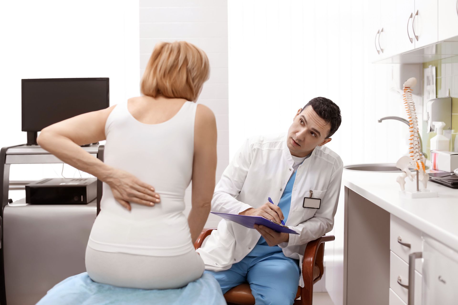 Woman holding her back while discussing a workplace back injury with a doctor in a medical exam room