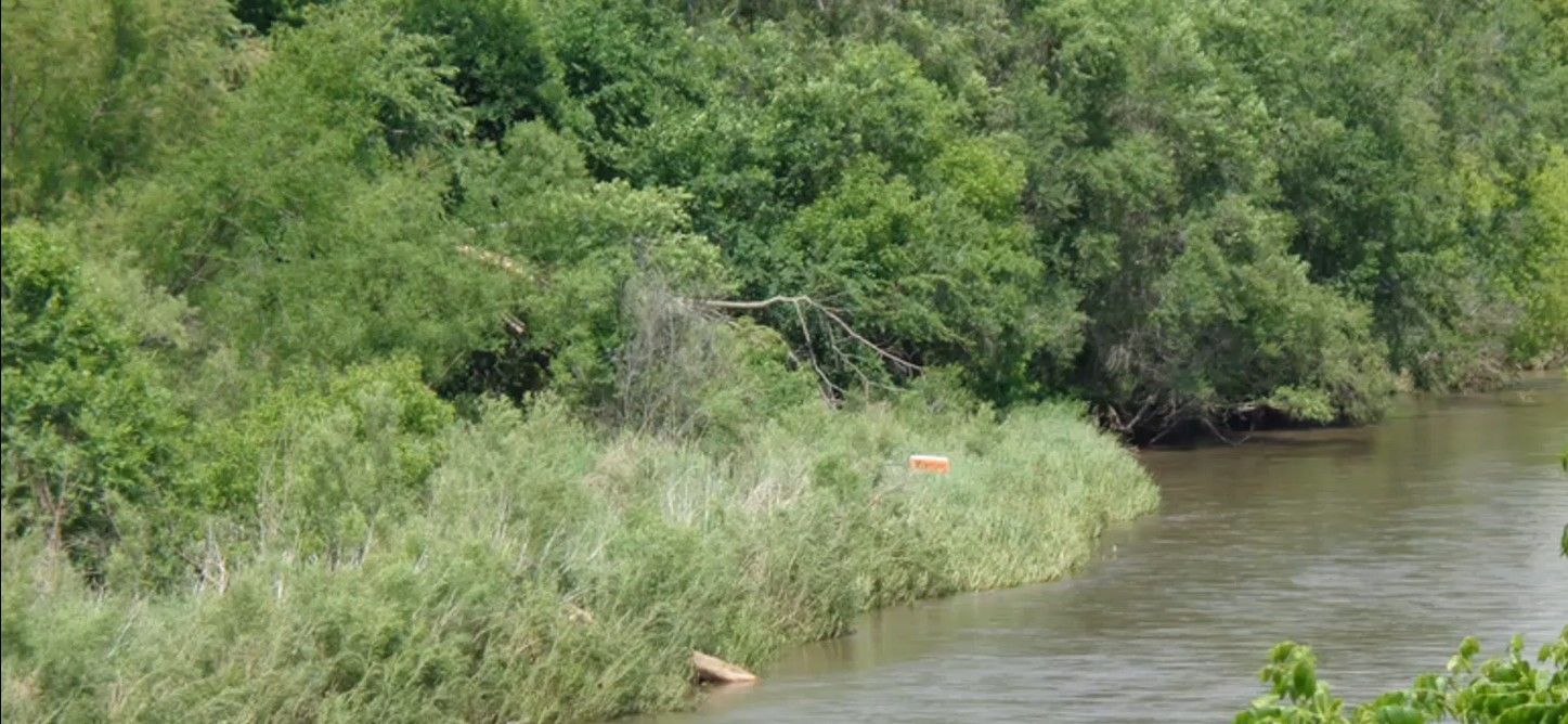 River with warning sign that is hidden by tall grass and weeds that caused a death of 2 Iowan's.