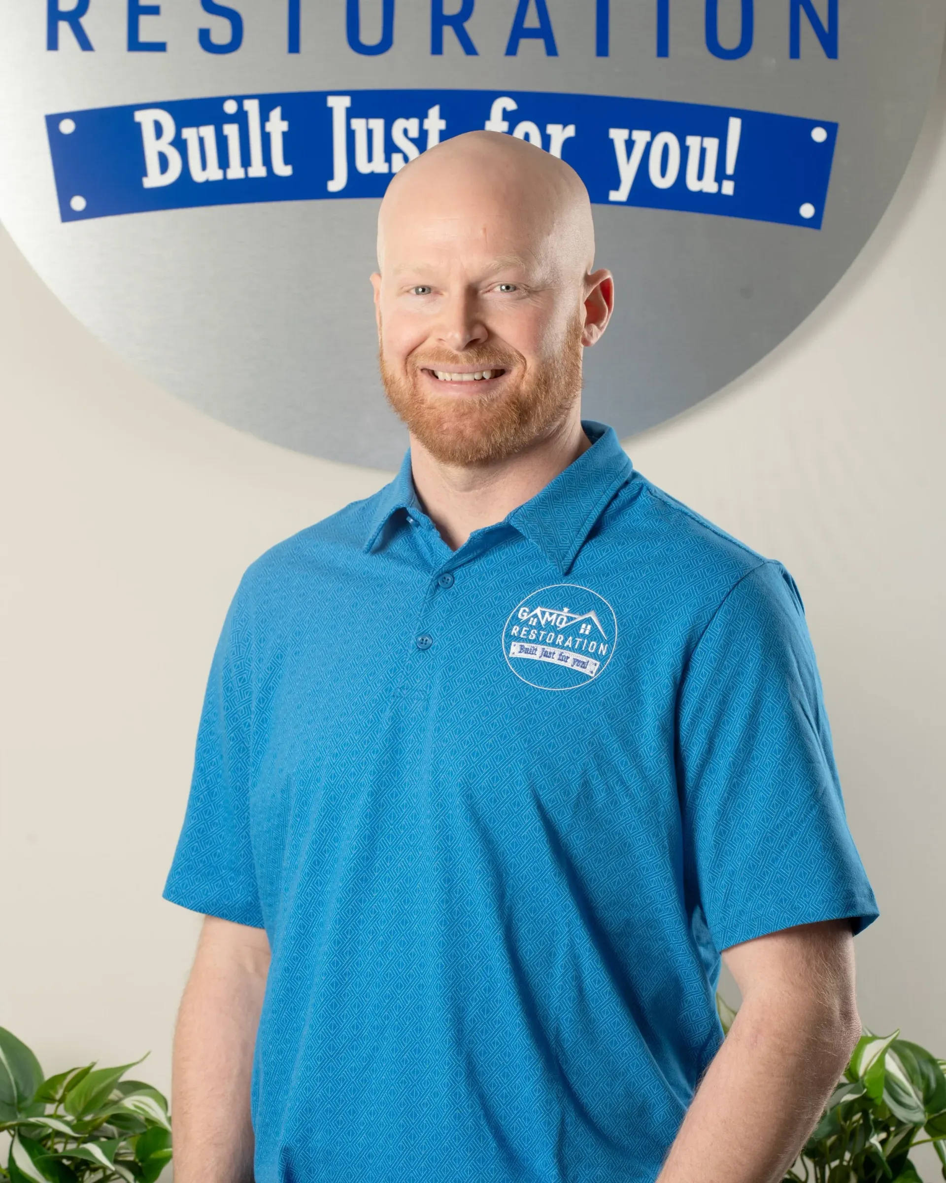 Man standing in front of a restoration sign, wearing a blue polo shirt and smiling