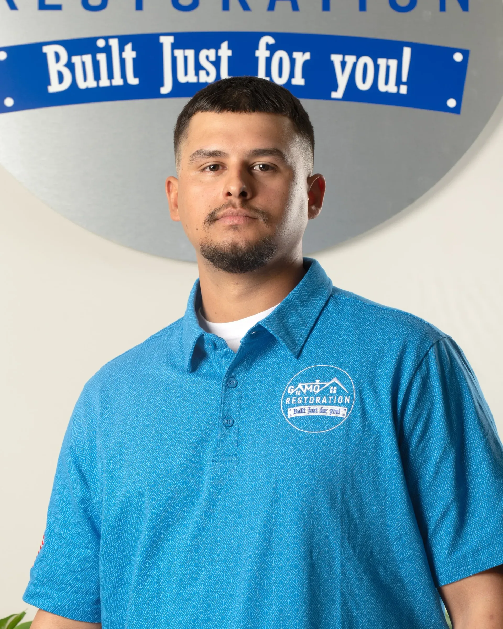 Man standing in a blue polo shirt in front of a sign reading “Built Just for You!”