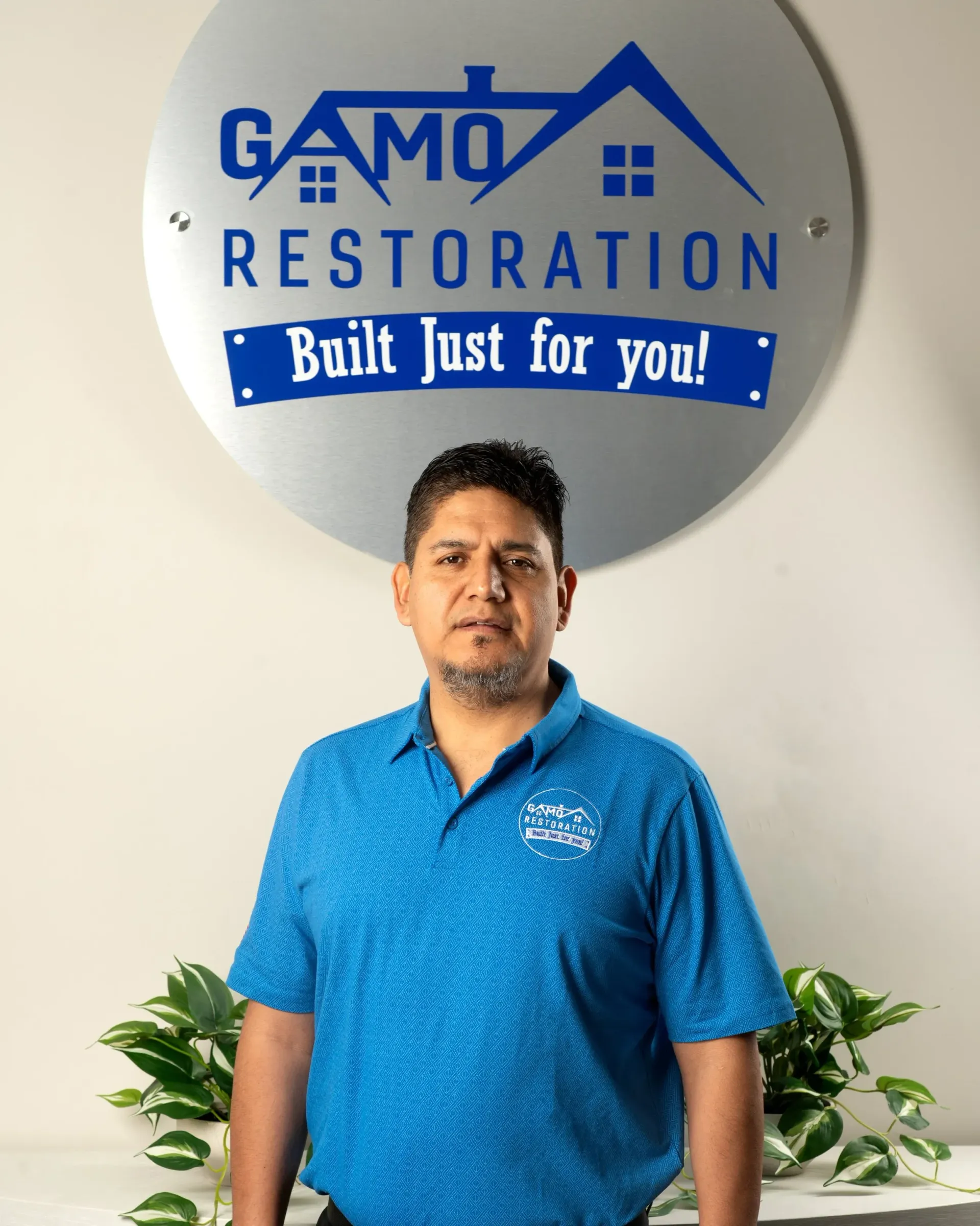 Man standing in front of a GAMO Restoration sign, wearing a blue polo shirt.