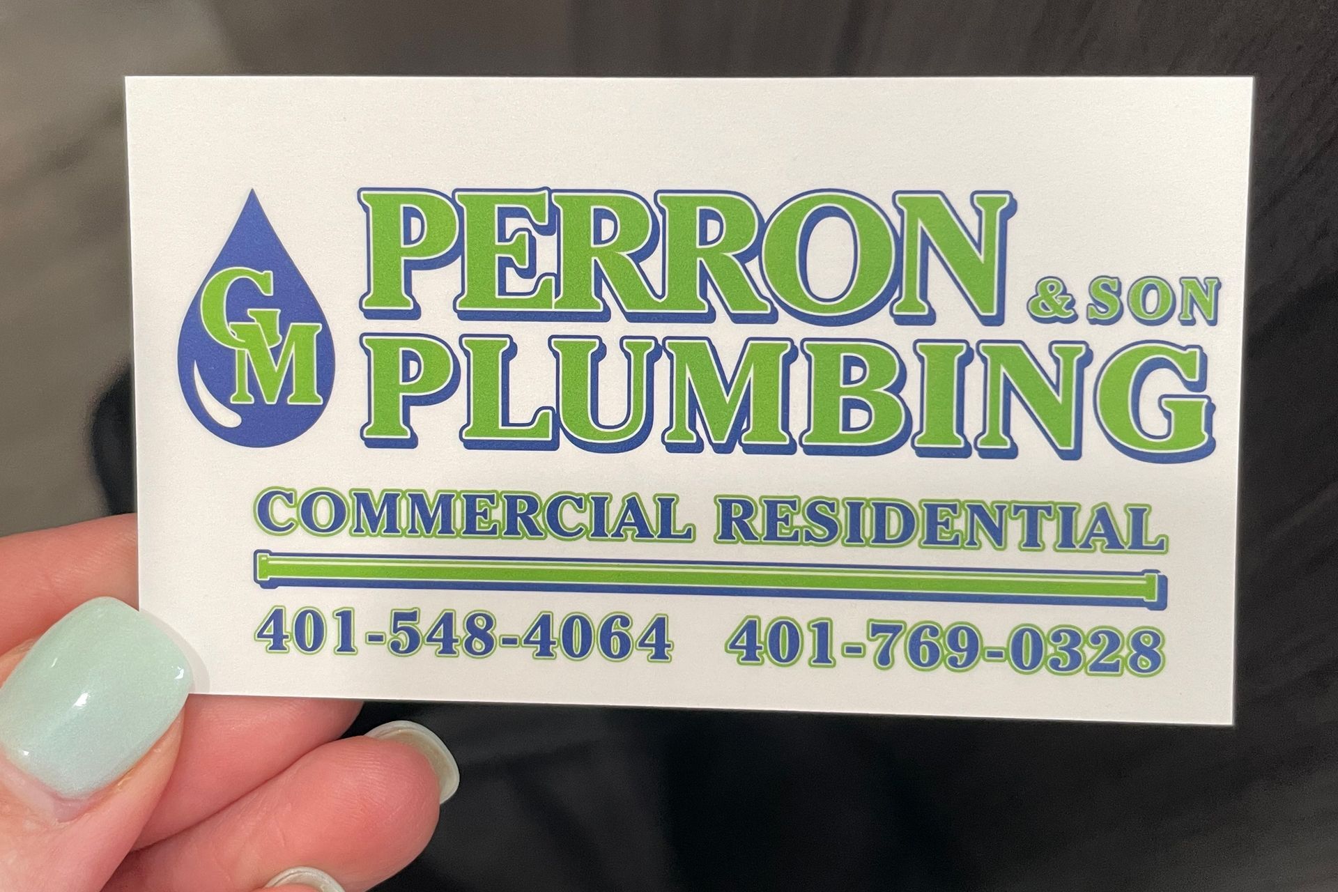 A person is holding a business card for GM Perron & Son Plumbing