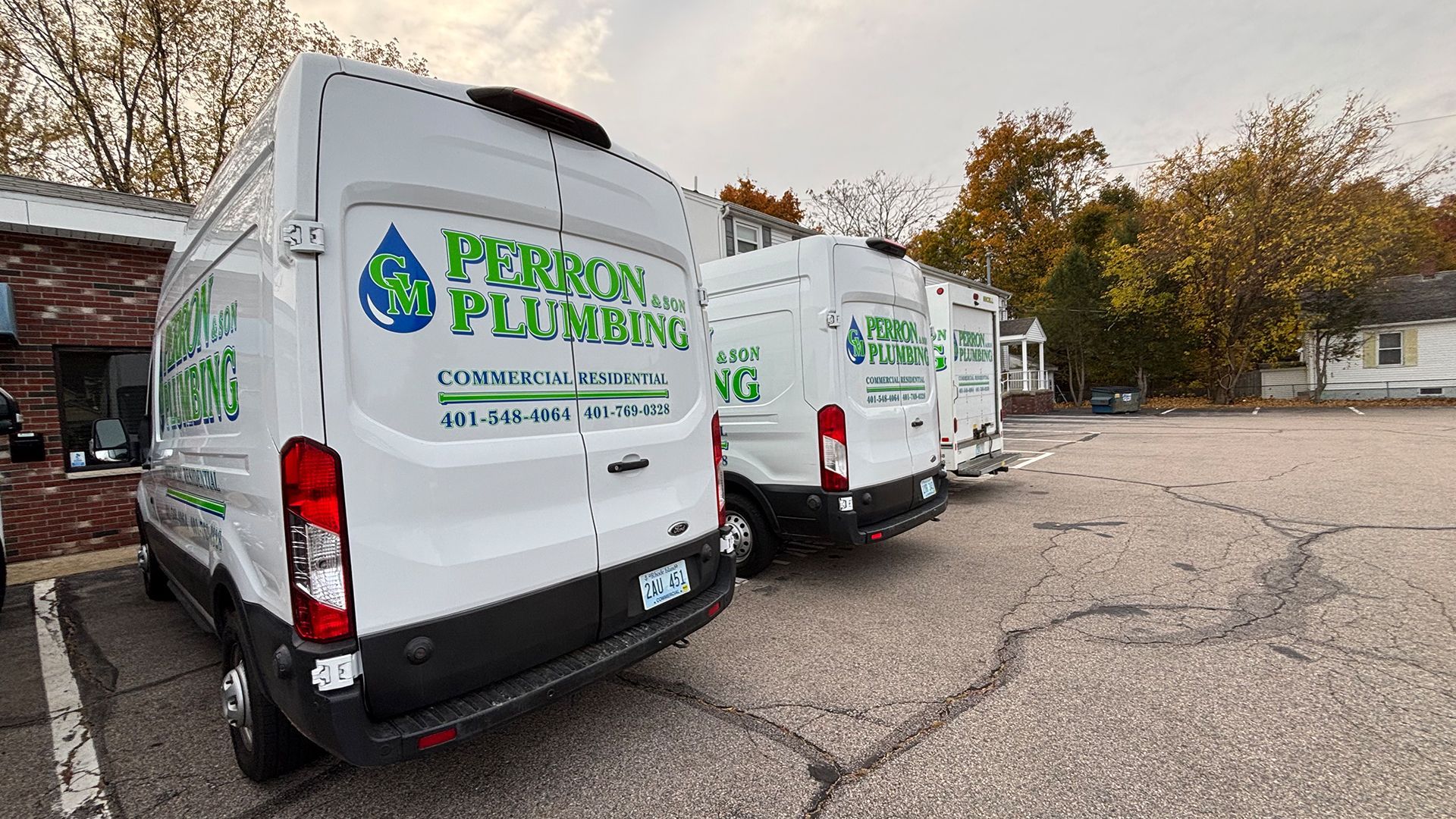 Three white Perron Plumbing vans parked in a cracked lot.