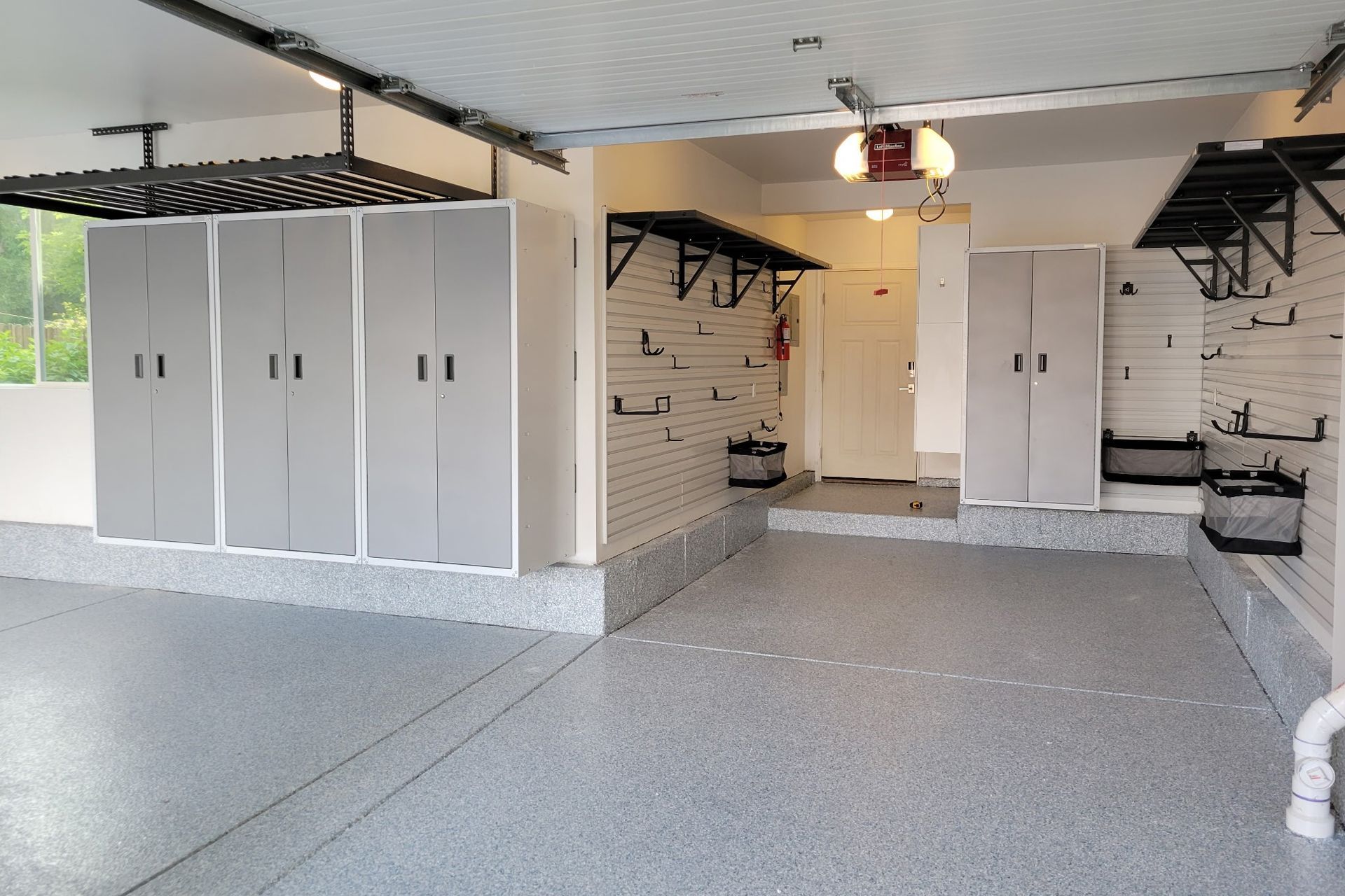 Spacious, organized garage with gray cabinets, shelving, and speckled flooring. A white brick wall and a closed white door are visible.