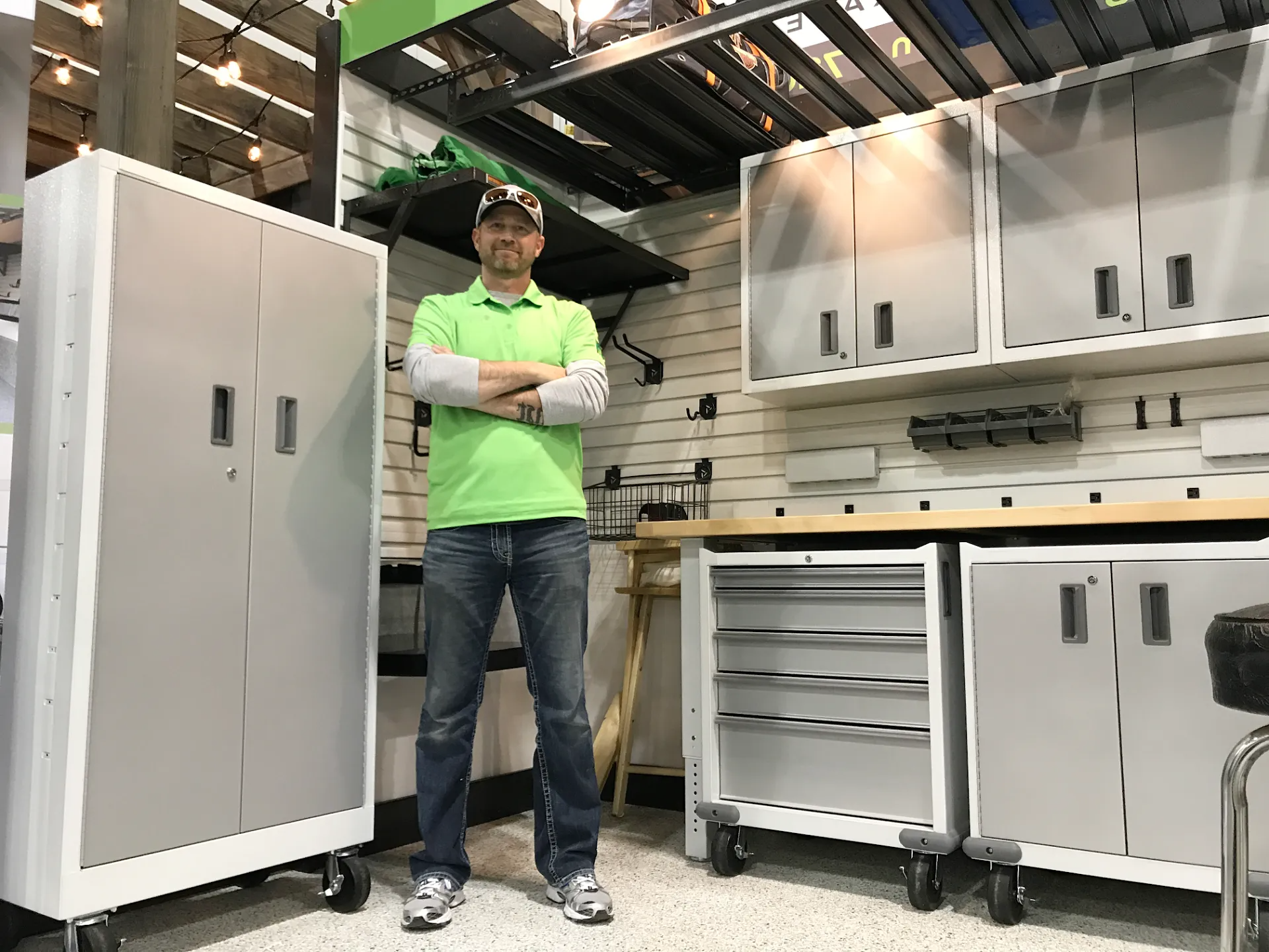 Man in a green shirt and jeans stands in a garage-like setting with silver storage cabinets.