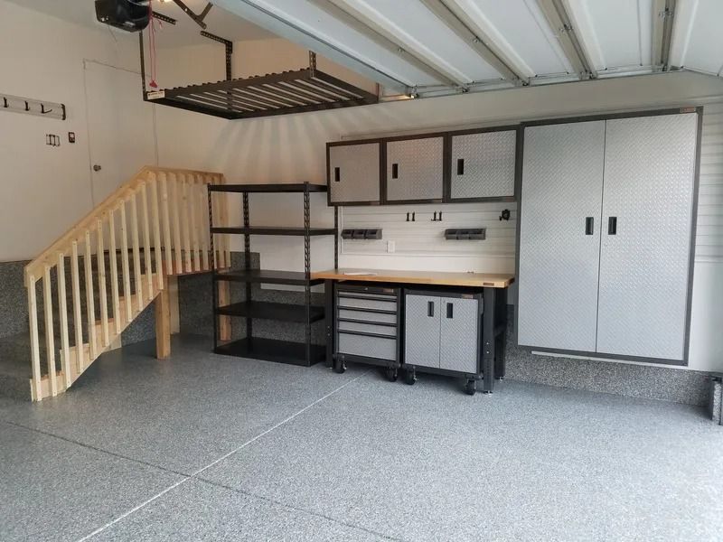 Garage with storage, workbenches, and stairs. Gray cabinets and speckled floor.