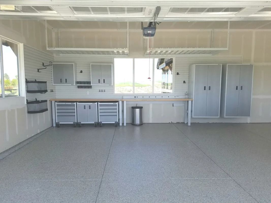 A garage with gray flooring, cabinetry, a workbench, and overhead storage.