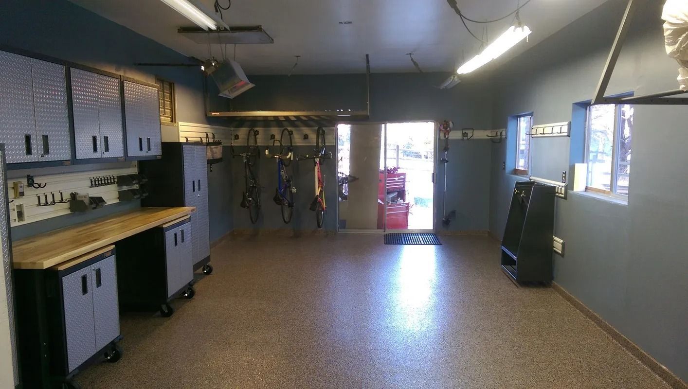 Organized garage with gray cabinets, a workbench, and bikes hanging near an open door.