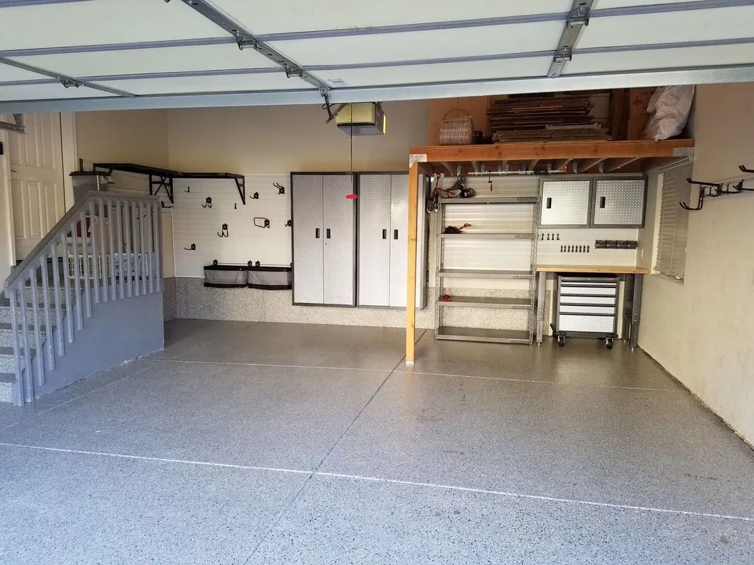 Empty garage with gray speckled floor, cabinets, and a work area.