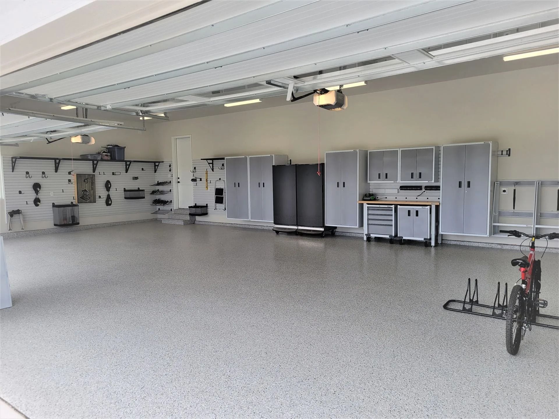 Spacious, organized garage with gray cabinets, tools on the wall, and a speckled floor. Bicycle in the corner.