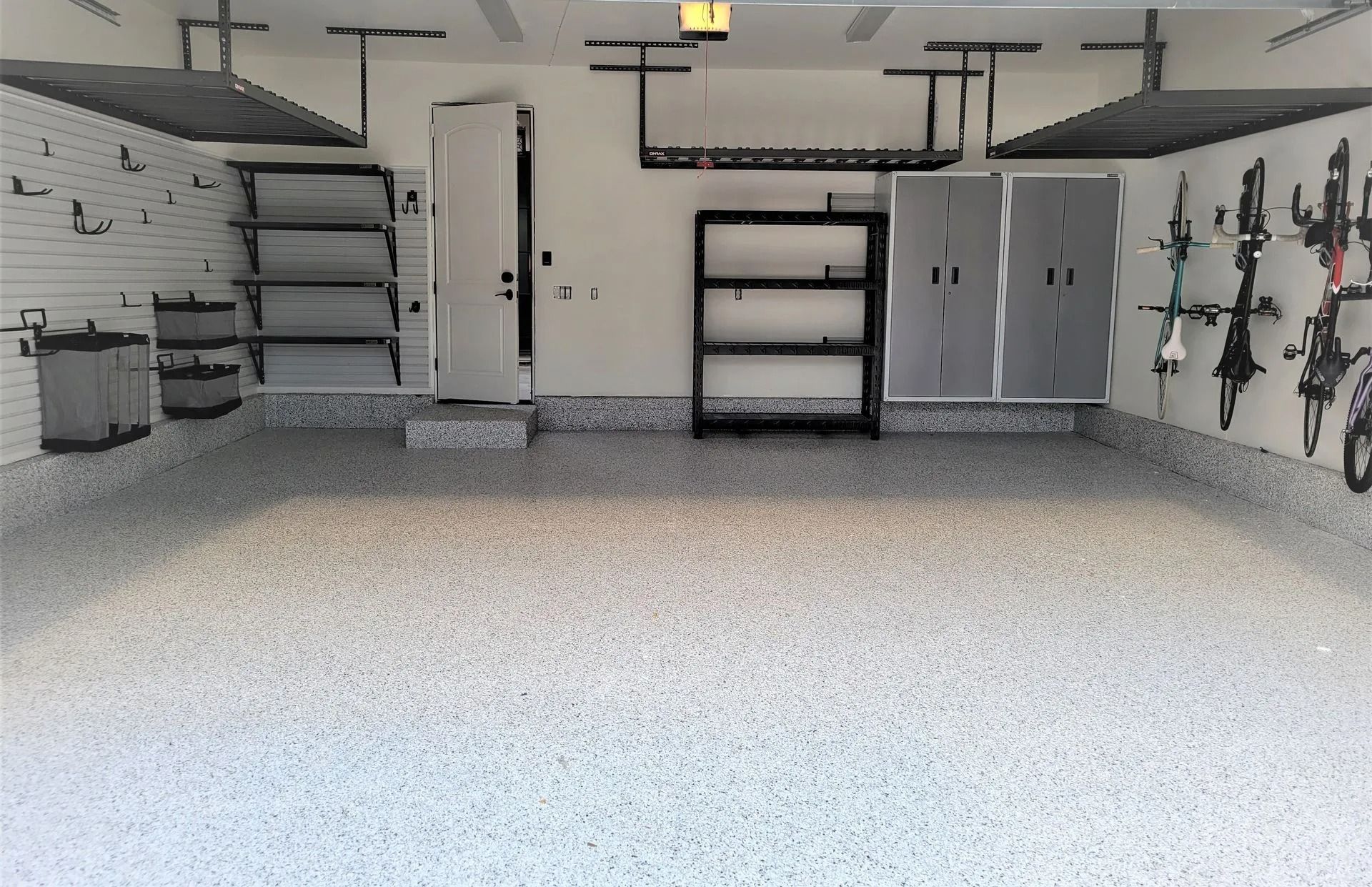 Clean, organized garage with epoxy floor, storage shelves, cabinets, and door.