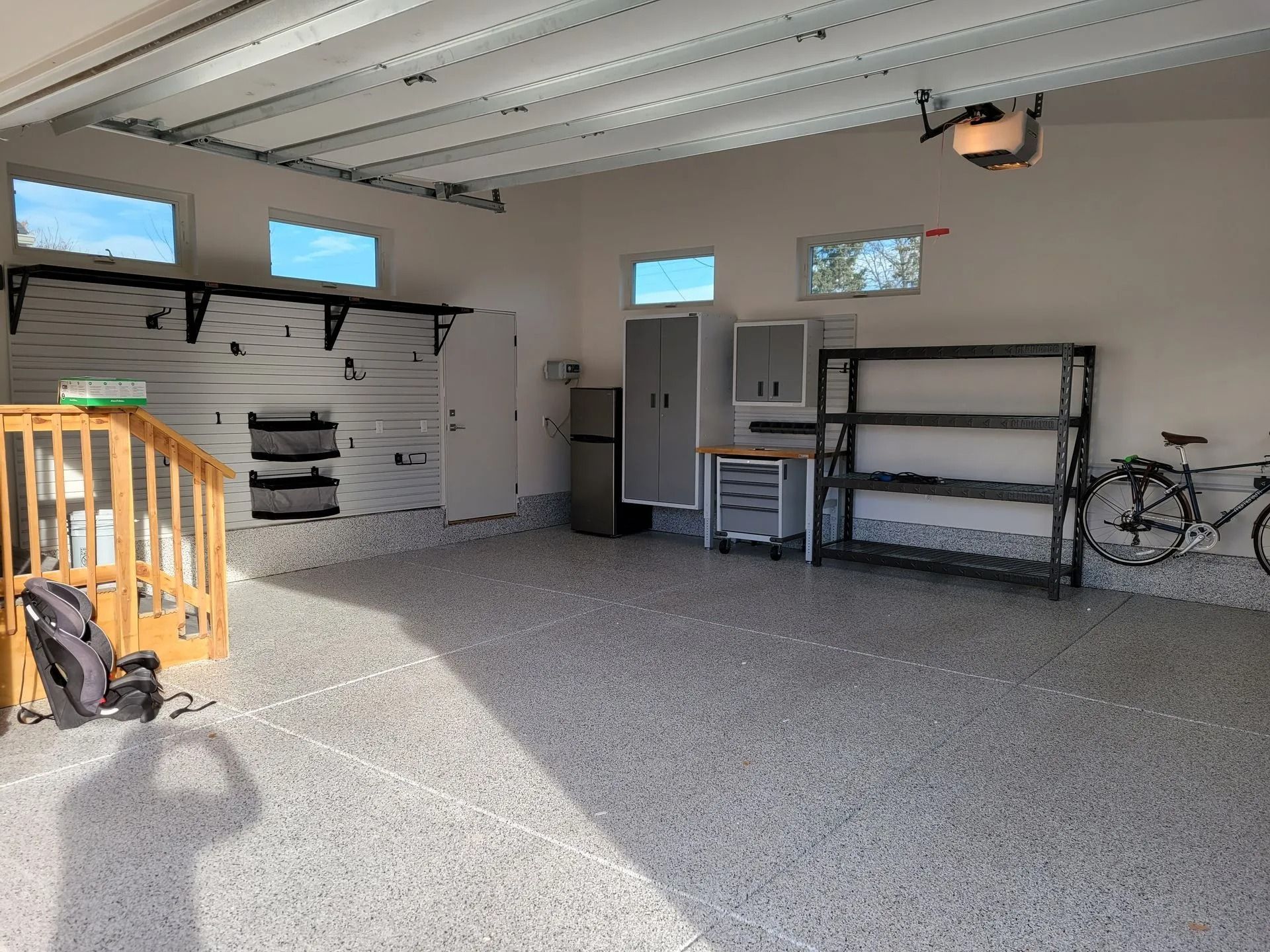 Spacious, well-lit garage with epoxy floor. Shelving, cabinets, and bike line the walls; sunlight streams in.