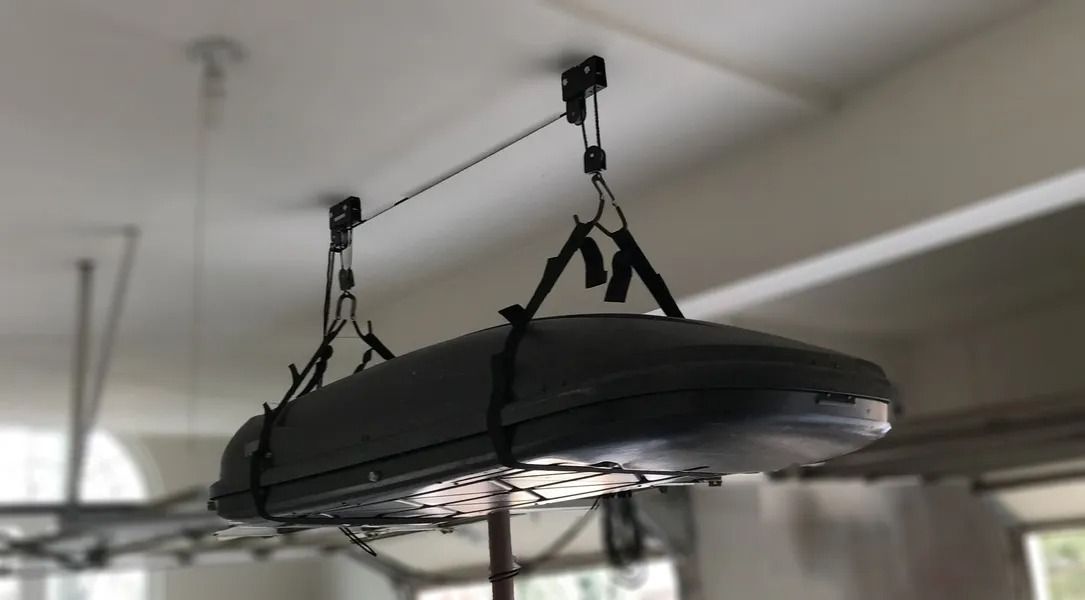 Gray car top carrier suspended from a ceiling using a pulley system.