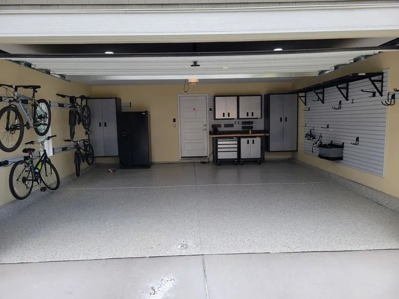 Garage interior with bikes, storage cabinets, workbench, and a garage door open.