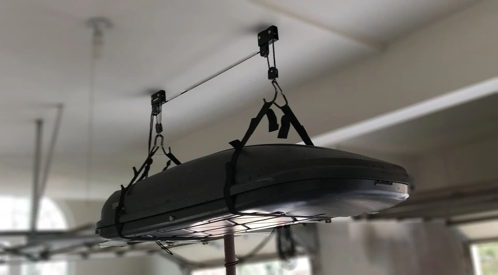 A car roof cargo box suspended from garage ceiling using a hoist system.