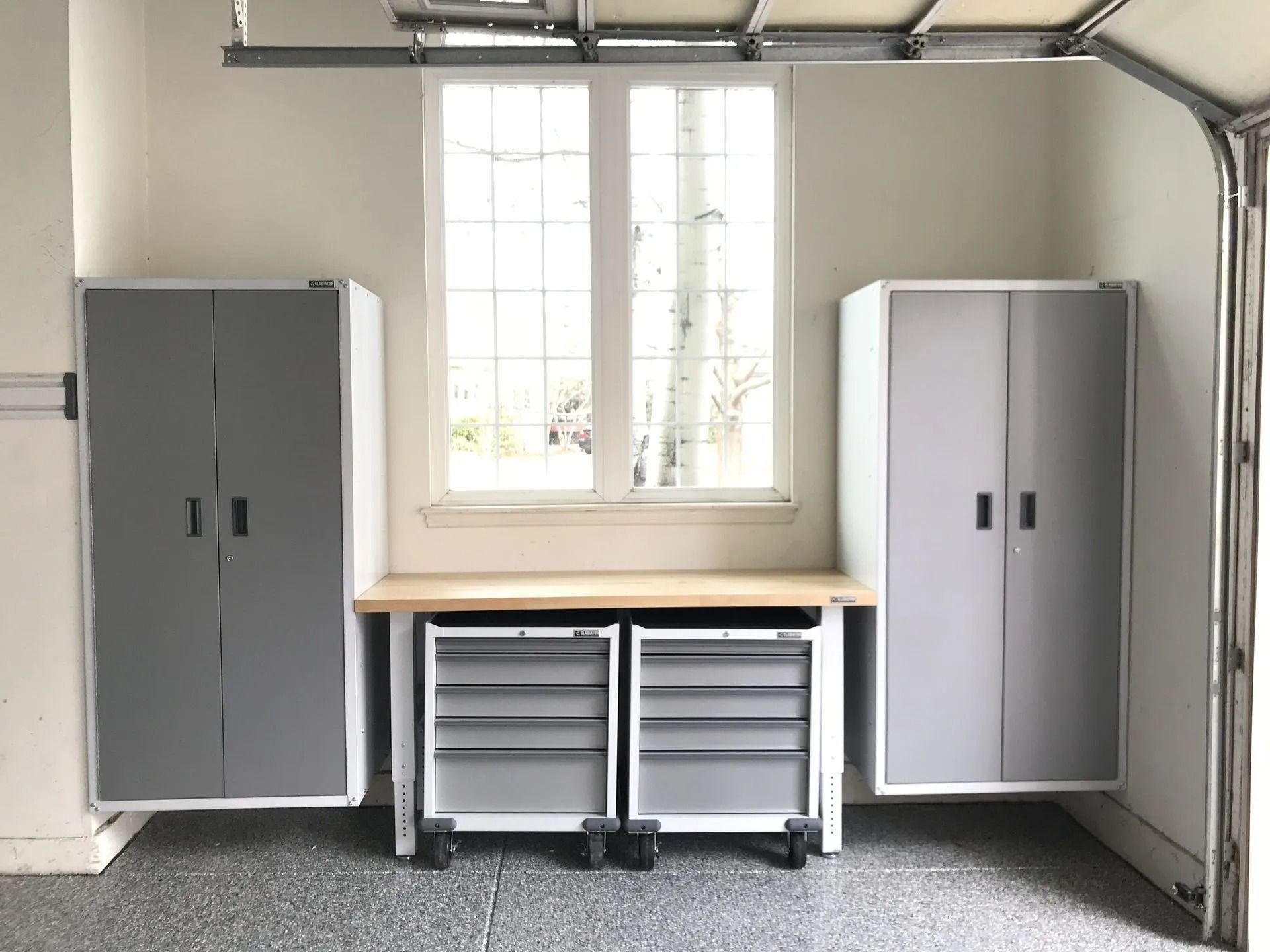 Garage organization: Grey cabinets, workbench with drawers, and window.