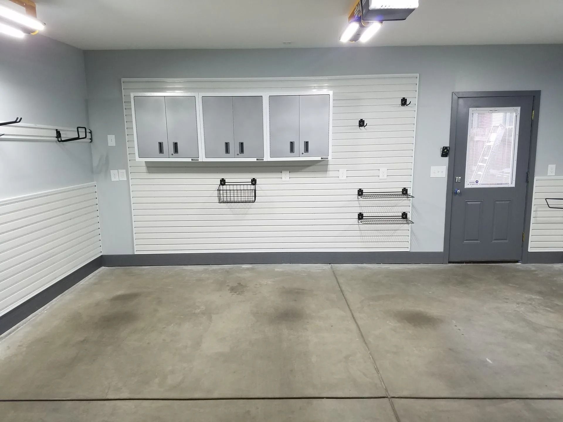 Garage interior with storage cabinets, slatwall, and a gray door.