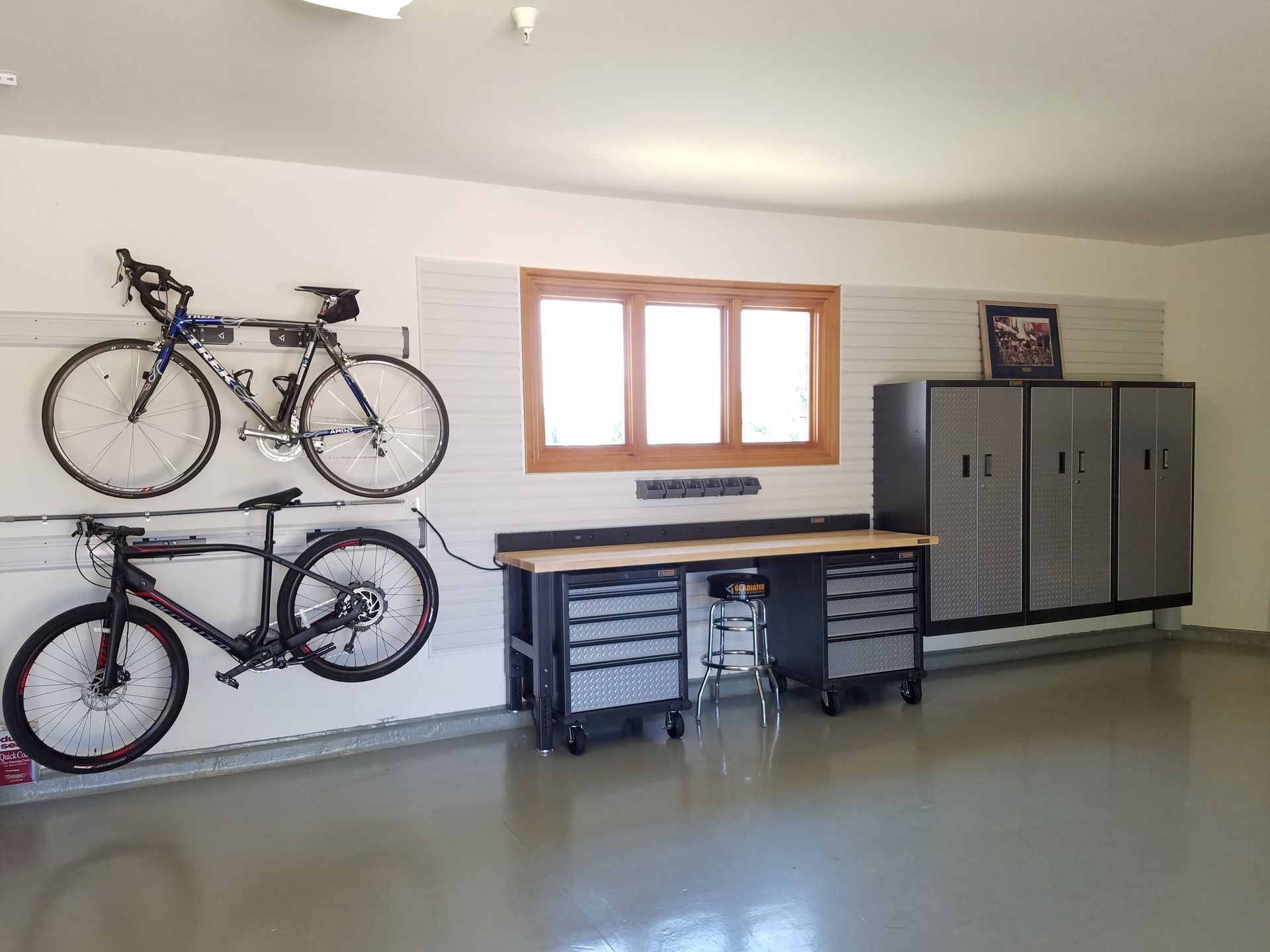 Garage with two bikes, a workbench, storage cabinets, and a window.