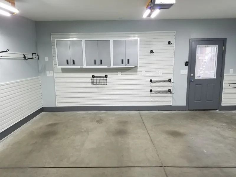 Empty garage with white slatwall, cabinets, door, and concrete floor.