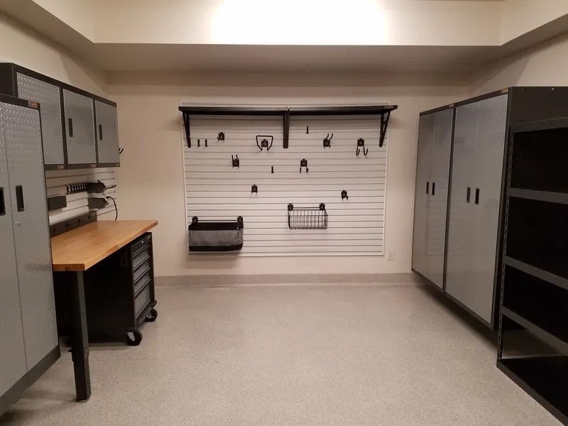 Garage with organized storage cabinets, work bench, and tool holders on a white wall.