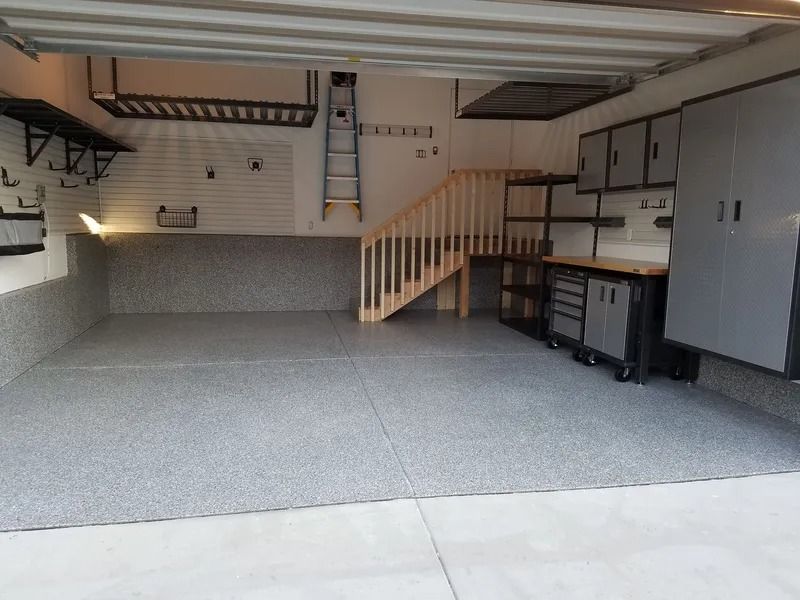 Spacious garage with gray epoxy floor, cabinets, stairs, and storage.
