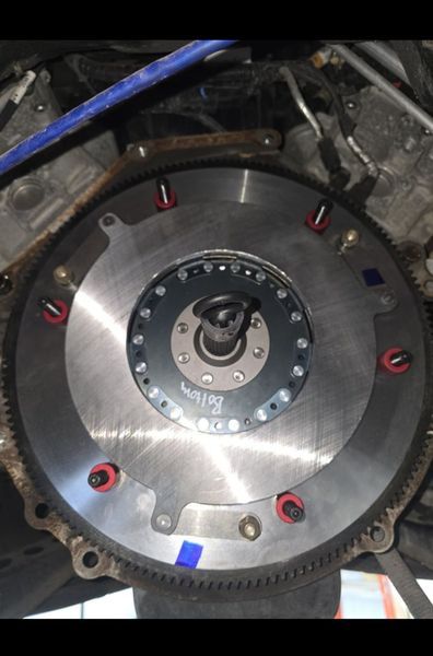 Engine flywheel with red bolts, mounted in a vehicle.