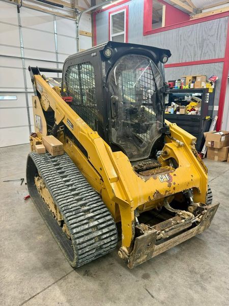 Yellow Caterpillar skid steer with tracks in a garage setting.