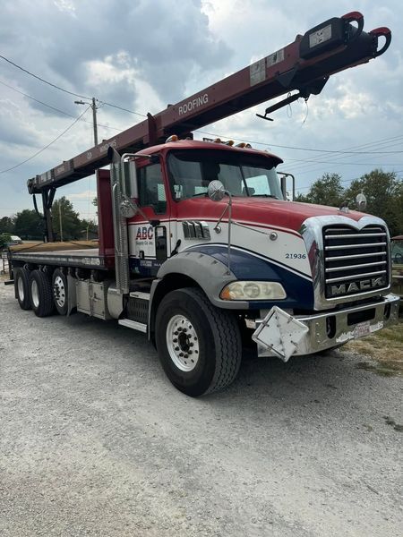 Red and blue Mack truck with crane on a gravel lot.