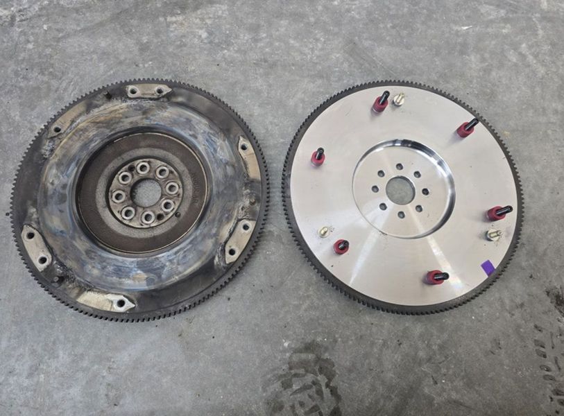 Two automotive flywheels, one worn, one new, side by side on a gray surface.