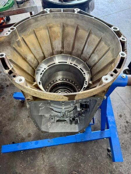 Transmission casing on a blue stand, showing internal components. Brown and silver. Workshop setting.