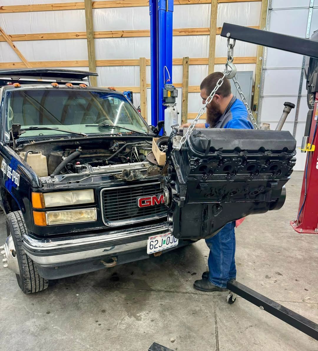 Mechanic removing an engine from a GMC truck with a hoist in a garage.