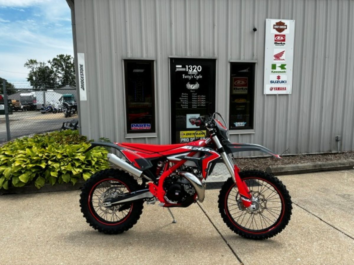 Red dirt bike parked outside a shop entrance on a concrete lot