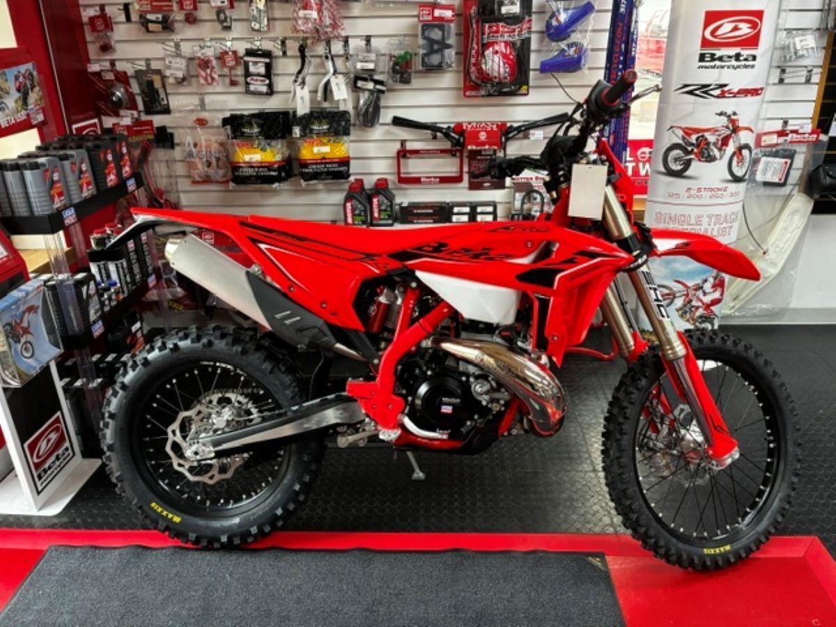Red dirt bike displayed in a showroom with accessories on wall shelves.