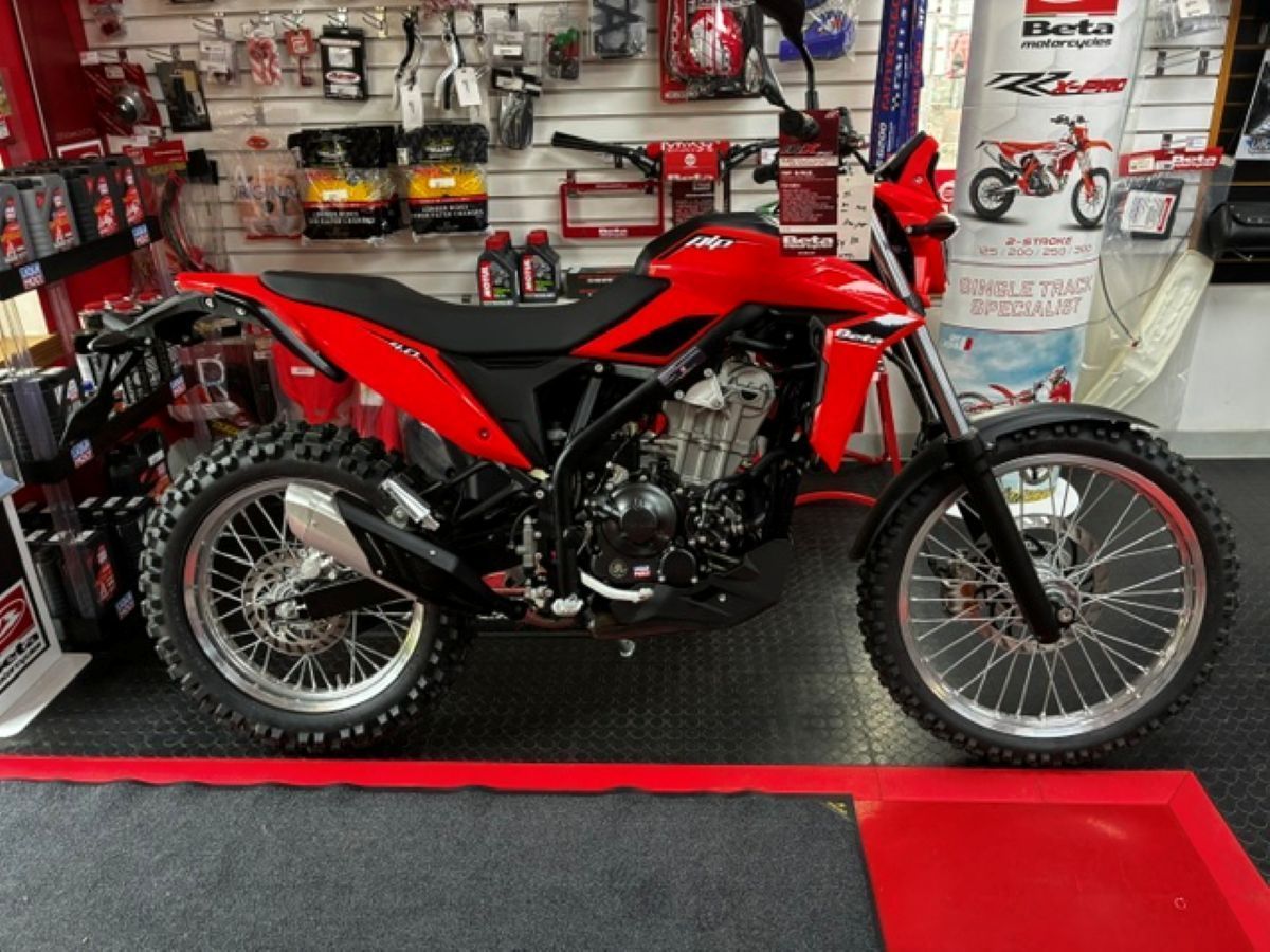 Red dirt bike on display in a motorcycle shop, with shelves of accessories in the background