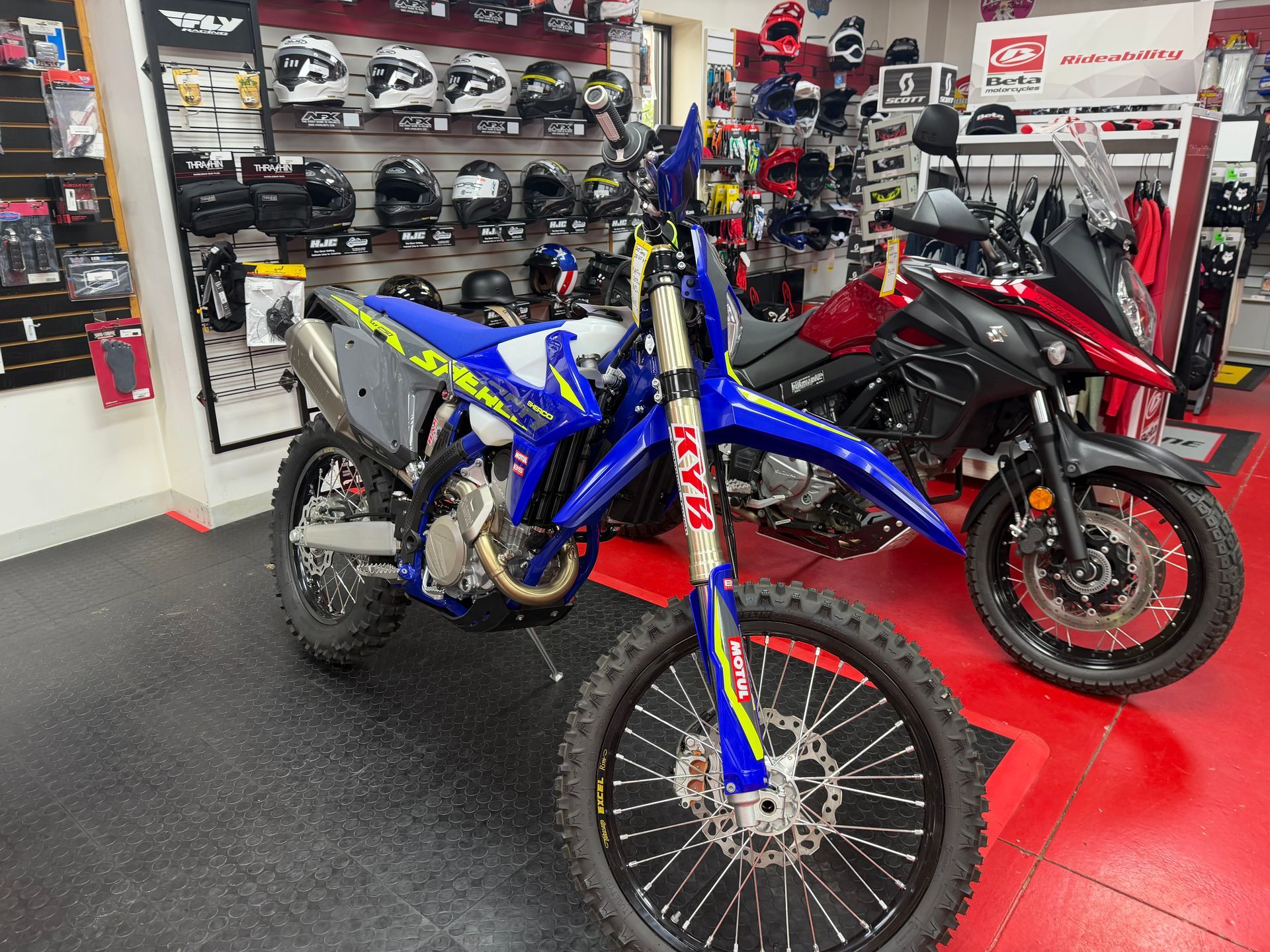 Blue dirt bike in a showroom beside a black and red sport bike on a red floor